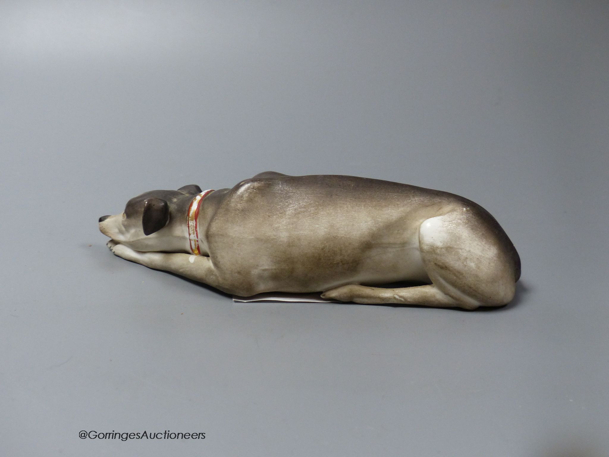 A Continental bisque reclining dog, 17cm